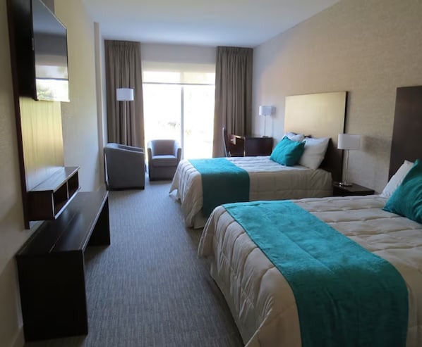 A hotel room with two beds, a desk, a chair, and a TV.