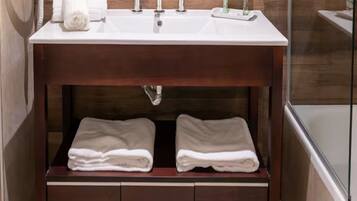Ein Badezimmer mit einem Holztischchen, einem Waschbecken, zwei Handtuchschubladen und einer Duschkabine aus Glas.