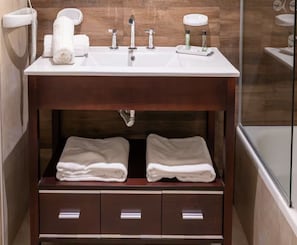 A bathroom with a wooden vanity, a sink, two towel drawers, and a glass shower enclosure.