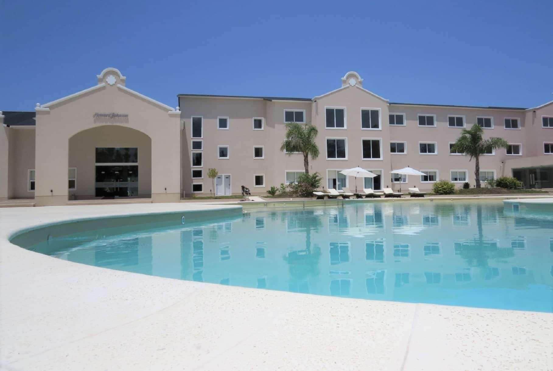 A hotel with a swimming pool, multiple balconies, and a clear sky.