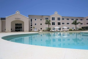 A hotel with a swimming pool, multiple balconies, and a clear sky.