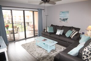 A living room with a sofa, coffee table, and a view of a balcony with outdoor furniture. - Sea Place 13137 2 Bedroom Condo (St. Augustine)