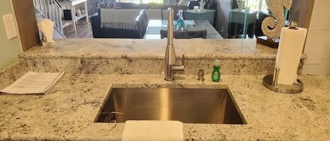 A kitchen with a granite countertop, stainless steel sink, and a towel hanging on the cabinet door.
