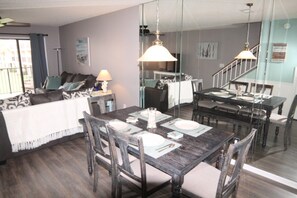 A dining area with a wooden table set for four, a sofa with cushions, a lamp, and a staircase leading to another level. - Sea Place 13137 2 Bedroom Condo (St. Augustine)