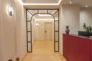 Uma área de recepção com piso de madeira, balcão de recepção vermelho e uma porta com placa de número.