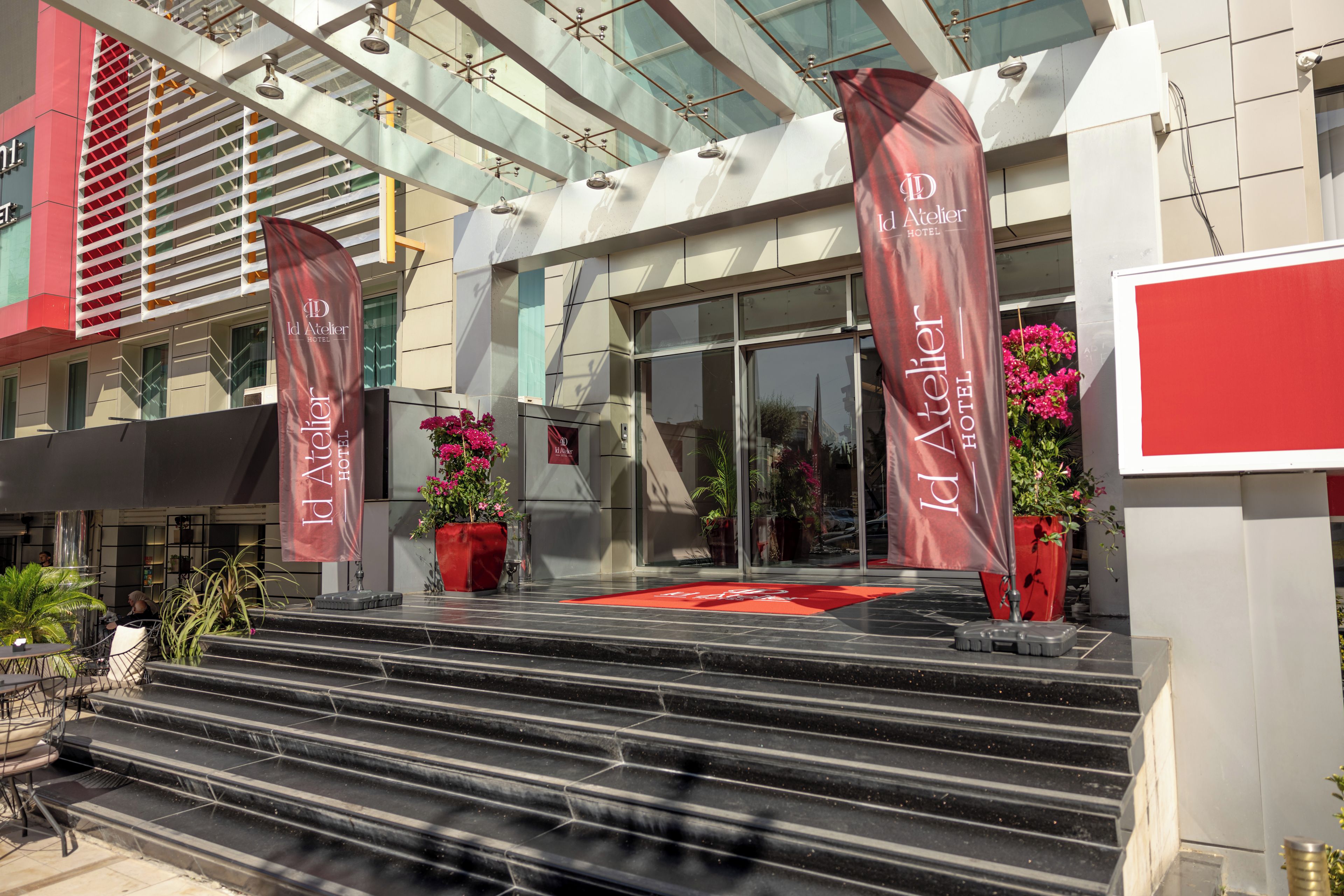 Fachada de hotel con paredes de vidrio, pancartas rojas y una alfombra roja que conduce a las puertas.