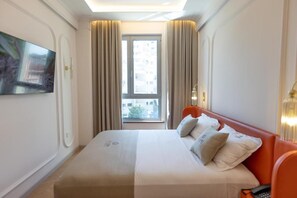 Quarto de hotel com cama, televisão na parede, janela com cortinas e vista exterior.