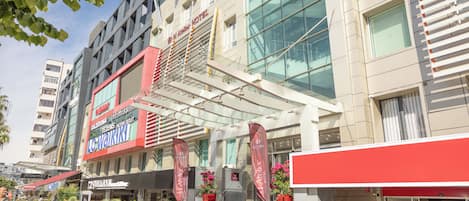 Un hotel con fachada moderna, varios pisos y un área exterior en la planta baja con mesas y sillas.