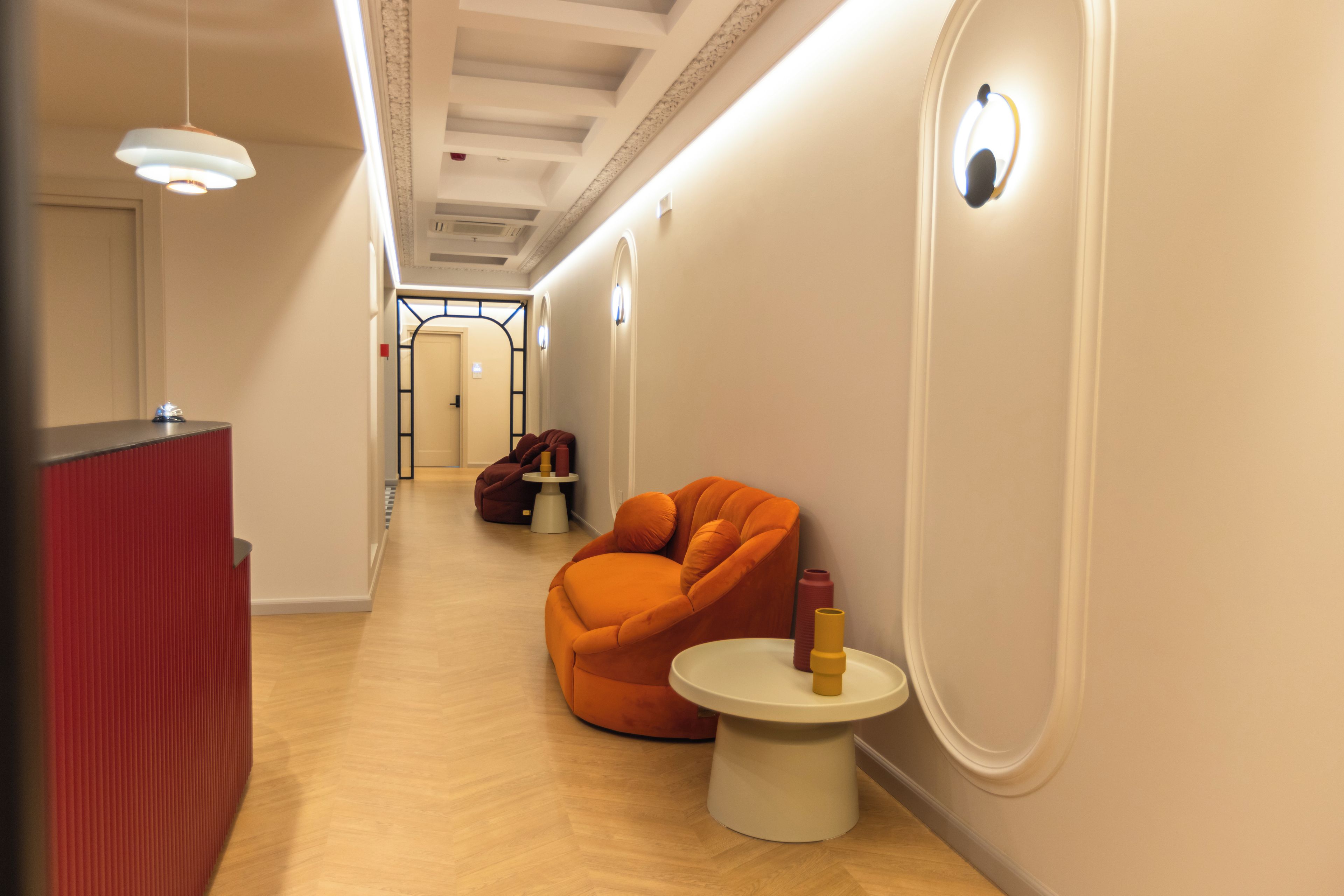 Un couloir avec un meuble rouge, une chaise orange et une petite table blanche sur laquelle se trouve un objet jaune.