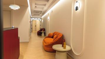 Un couloir avec un meuble rouge, une chaise orange et une petite table blanche sur laquelle se trouve un objet jaune.