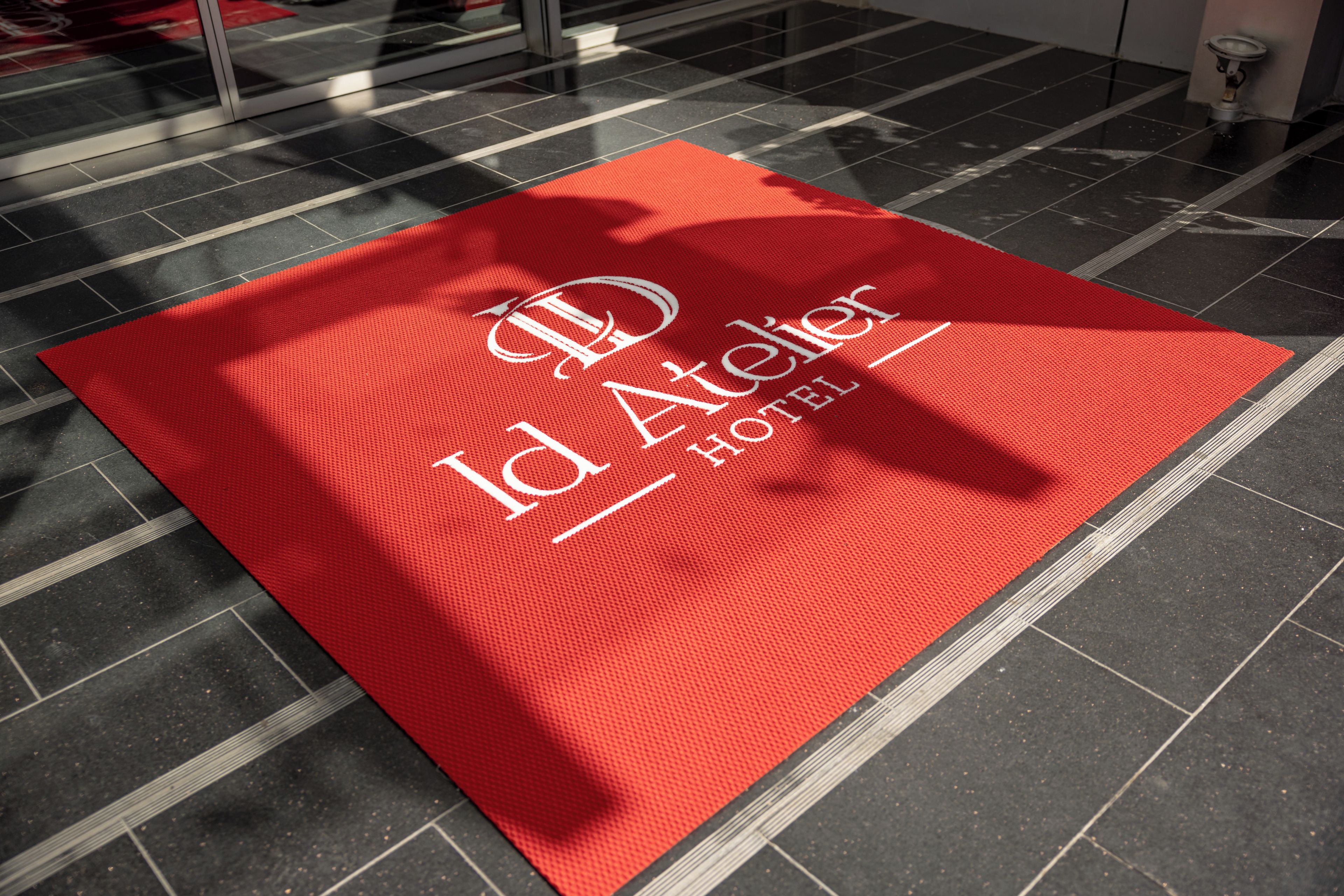 Eine rote Fußmatte mit dem Logo und dem Namen des Hotels.
