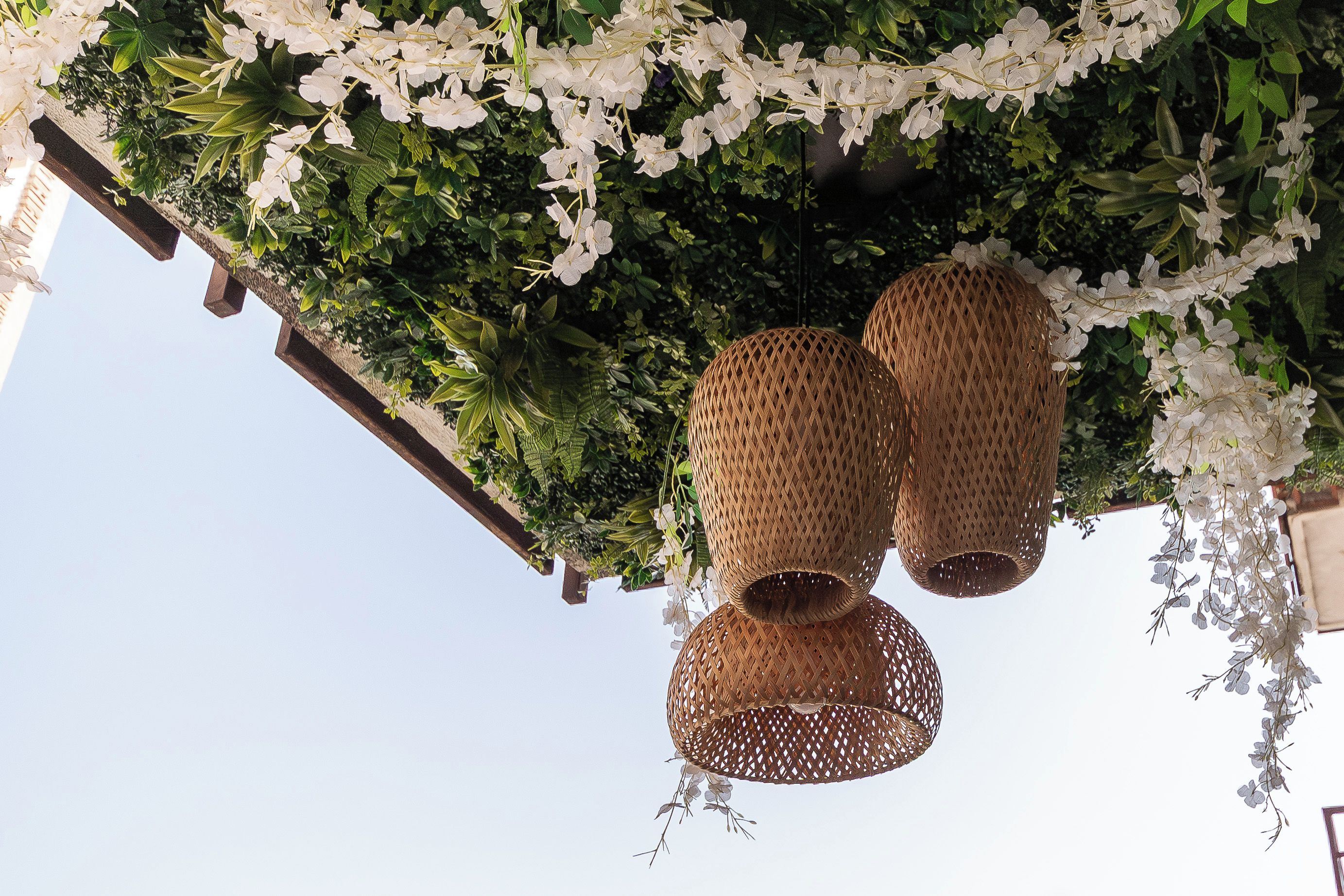 En hängkorg med vita blommor och två flätade lyktor.