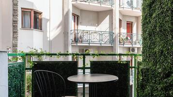 A courtyard with a table and chairs, surrounded by a hedge and a building with balconies.