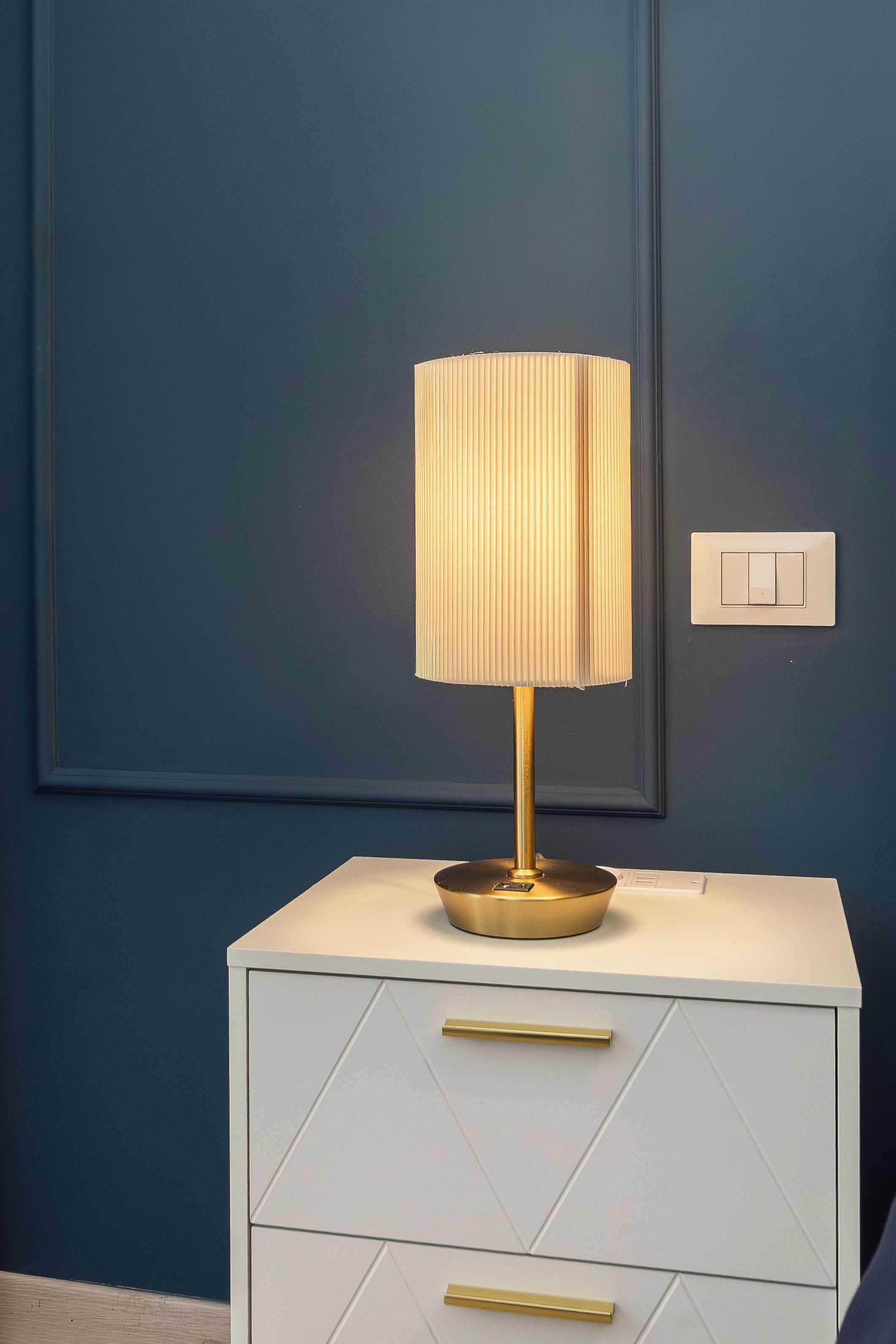 Ein Nachttisch mit Lampe, einer Schublade und einem Lichtschalter an der Wand.