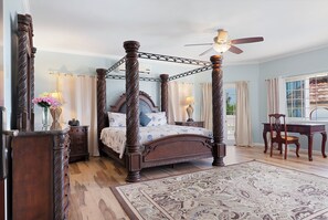 A four-poster bed with a ceiling fan, a desk, and a chair in a room with patterned carpet. - Hospitality Expert VSV BF 3BR Chef Pool  (Montego Bay)
