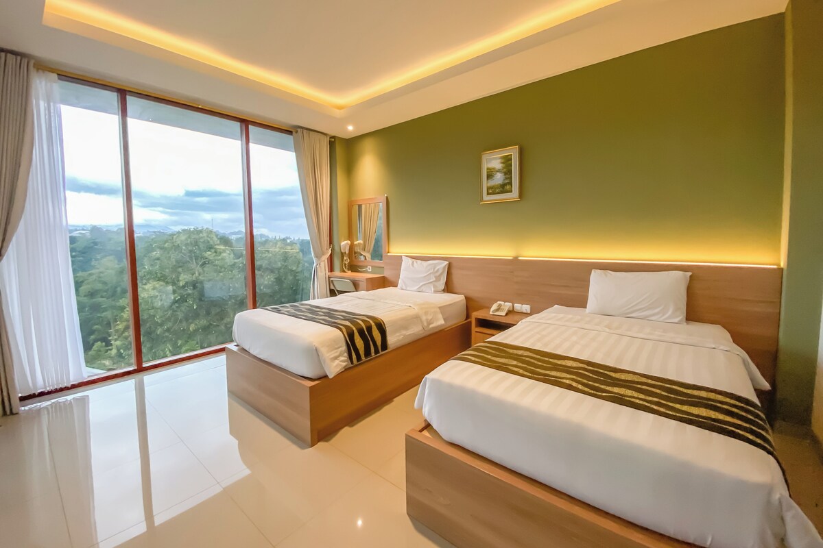 A hotel room with two beds, a desk, a phone, and a view of the outdoors.