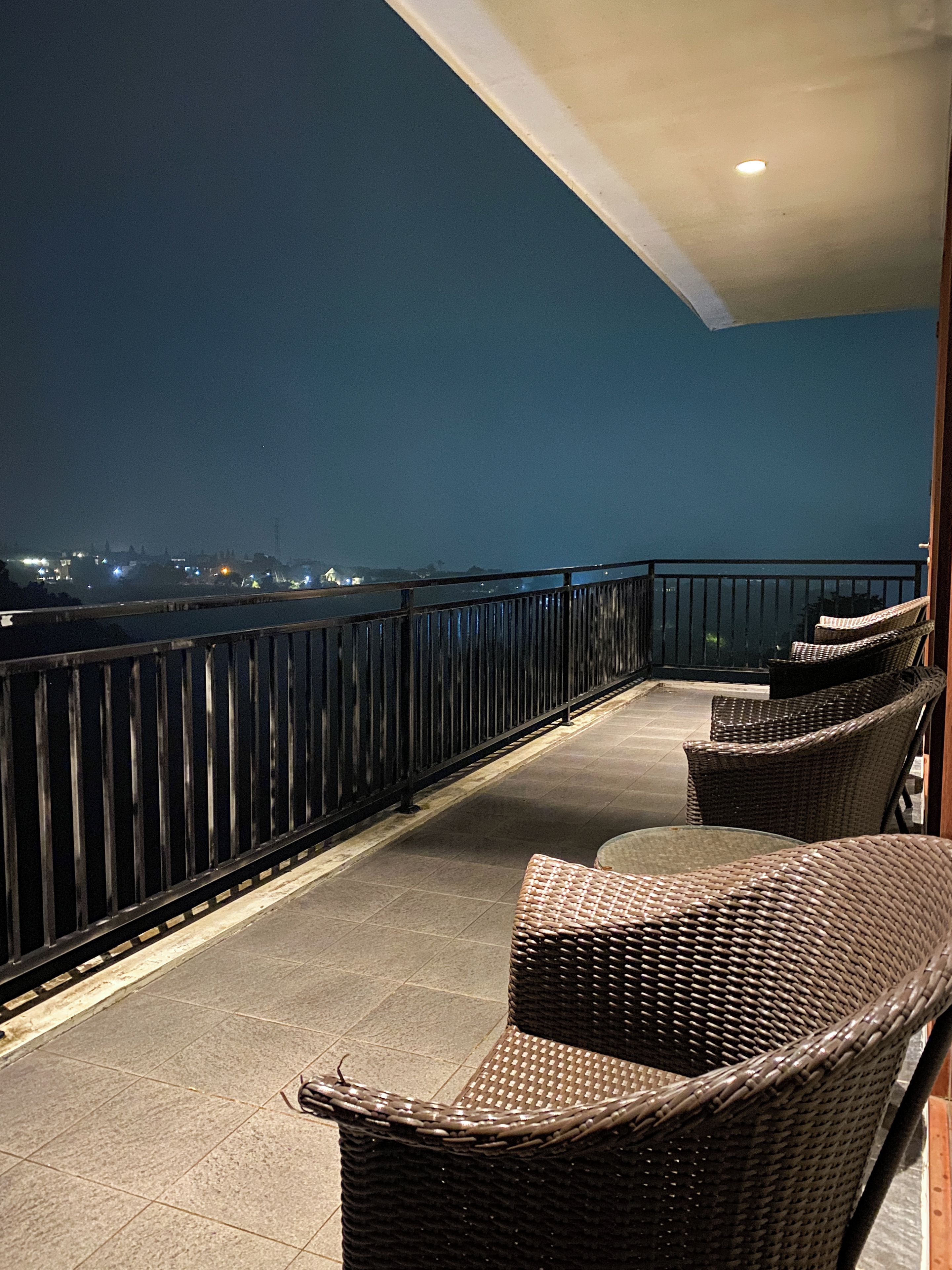 A balcony with wicker furniture, a railing, and a view of a cityscape at night.