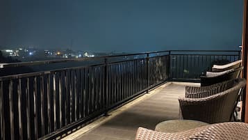 A balcony with wicker furniture, a railing, and a view of a cityscape at night.