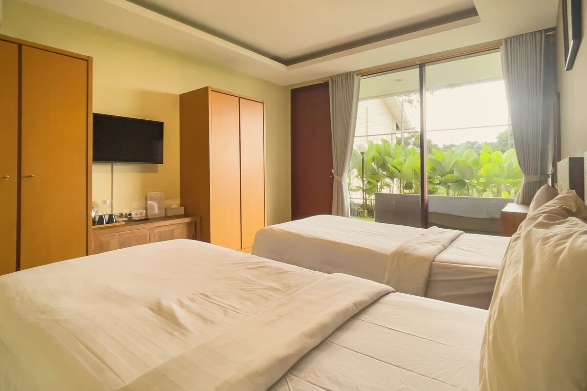 A hotel room with two beds, a television, a desk with a coffee maker, and a window with curtains.