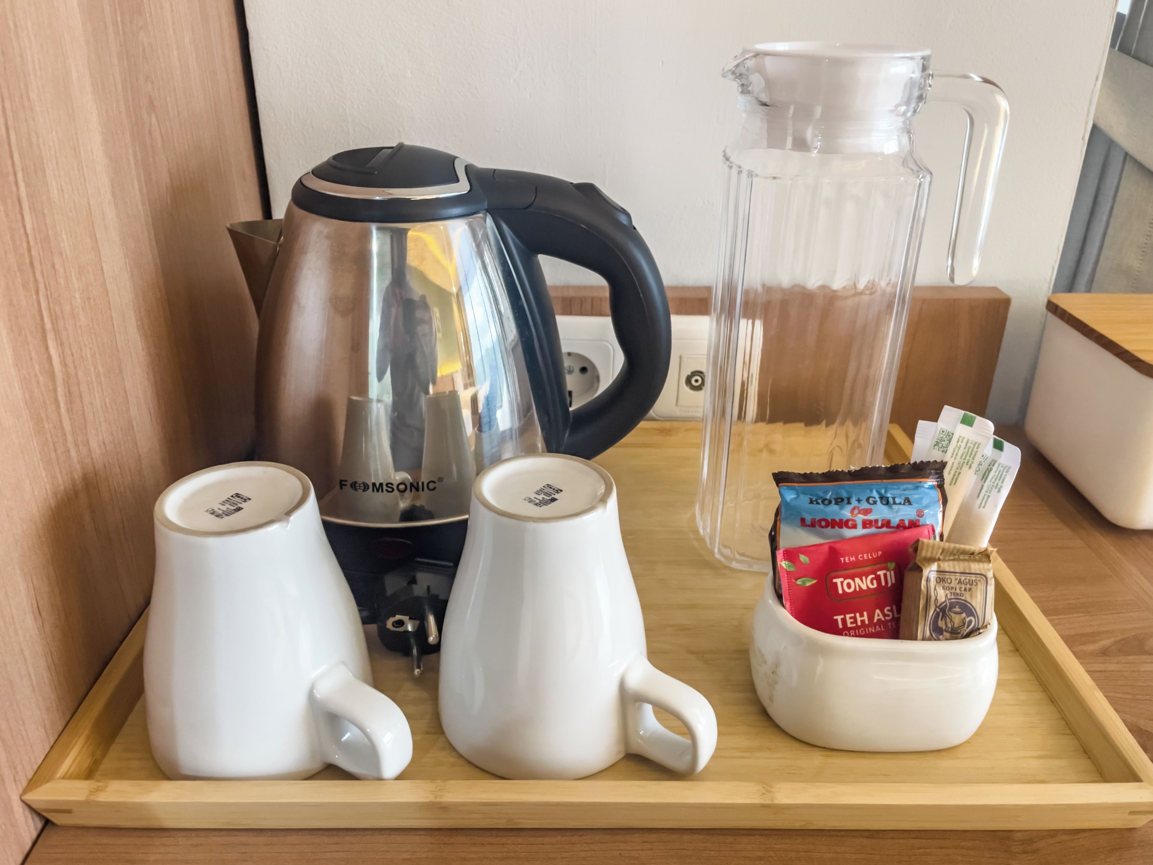A tray with two white mugs, a black and silver electric kettle, a glass pitcher, and a mug containing tea packets.