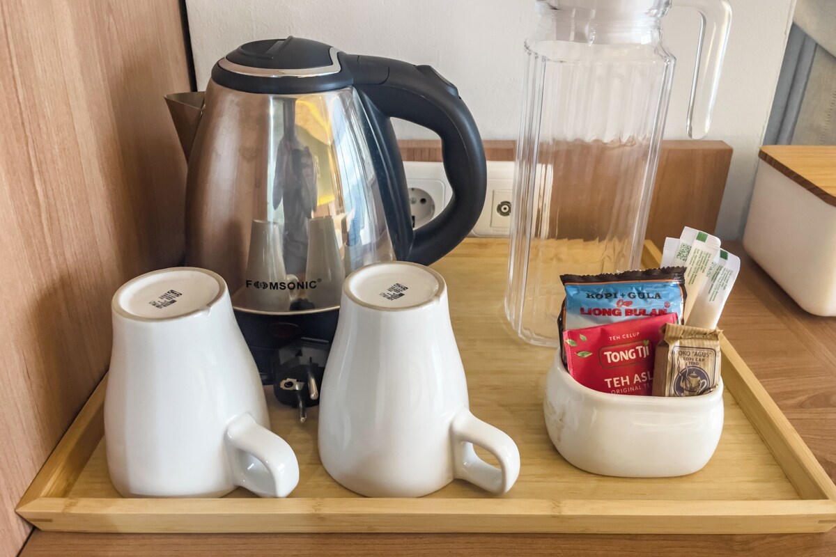 A tray with two white mugs, a black and silver electric kettle, a glass pitcher, and a mug containing tea packets.