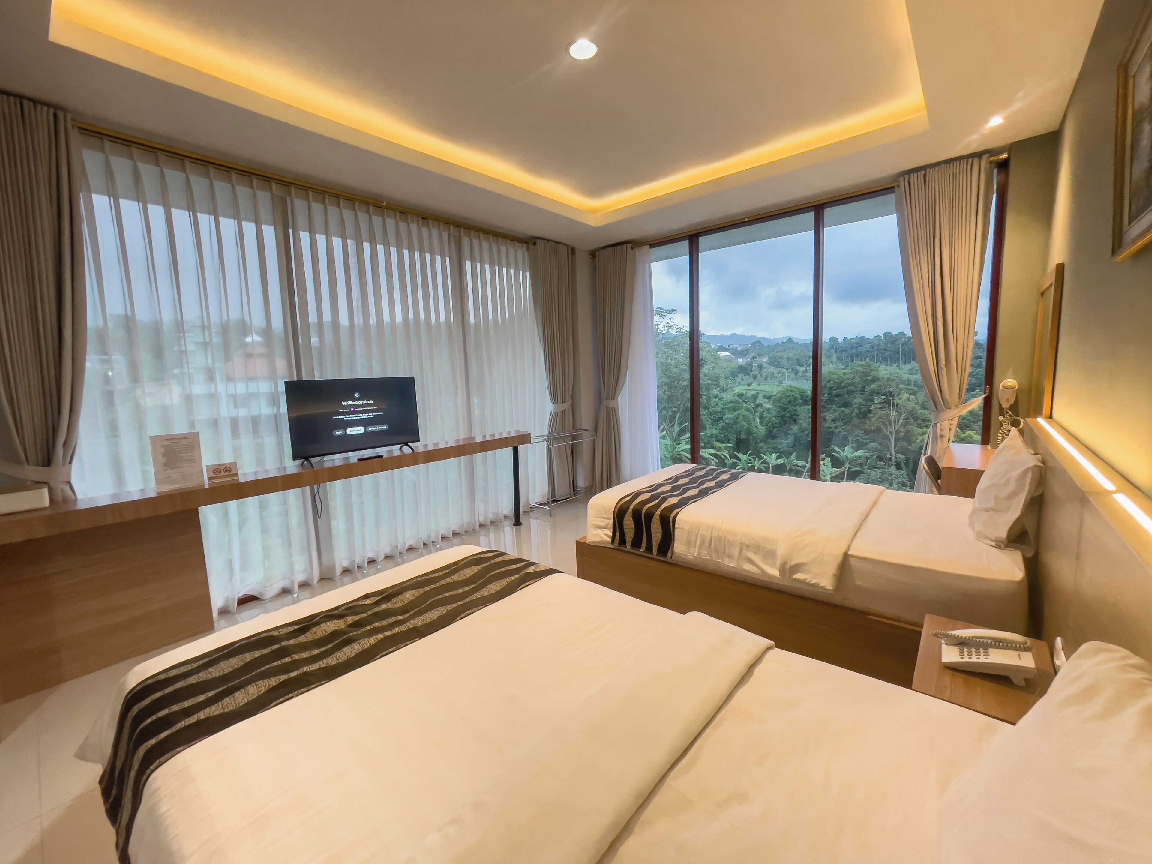 Ein modernes Hotelzimmer mit zwei Betten, einem Fernseher und einem großen Fenster mit Blick auf den Wald.