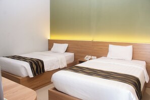 A hotel room with two single beds, a wooden nightstand with a telephone, and a small table. - RUKUN Place Bandung  (Kota Bandung)