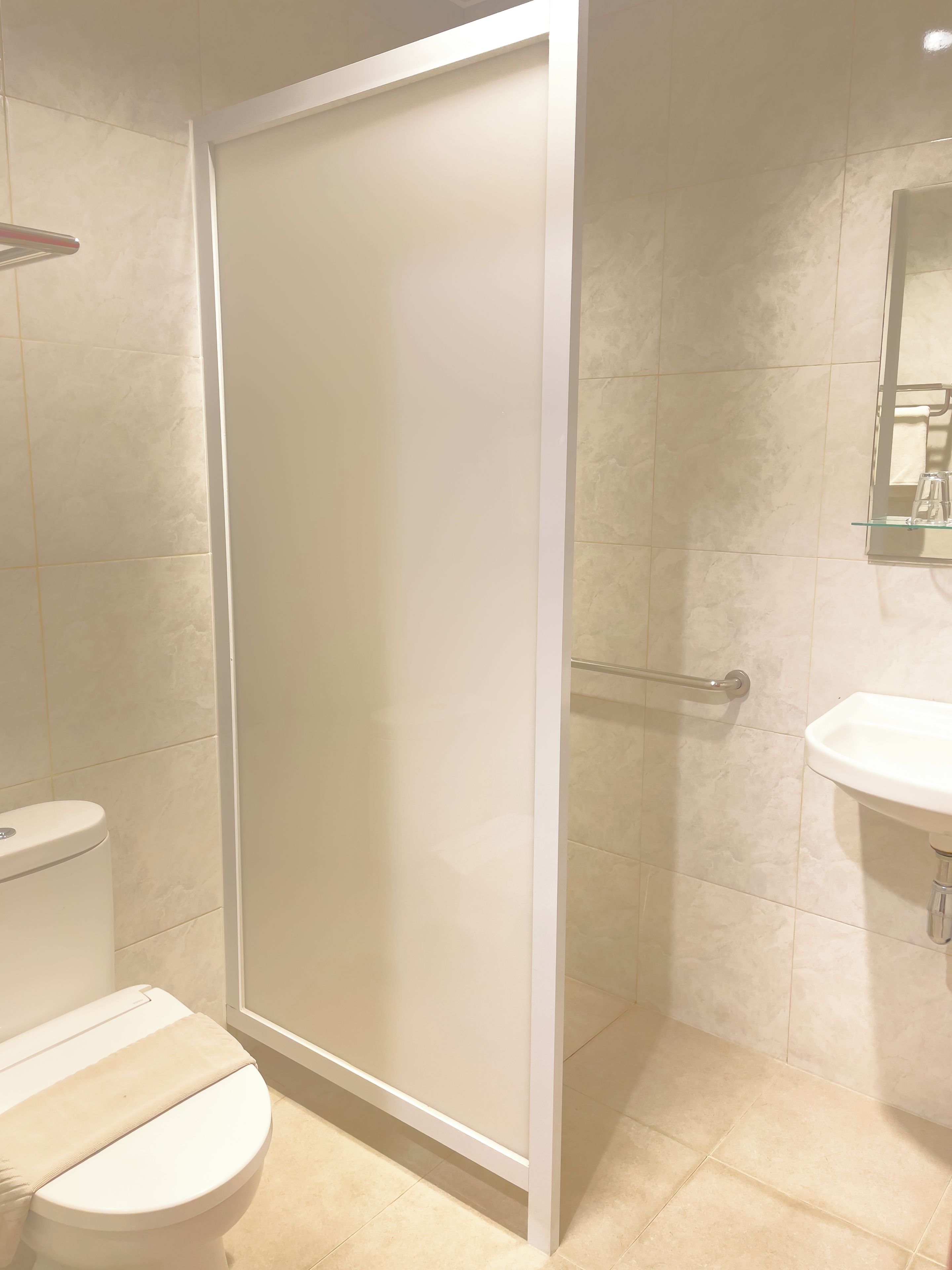 Un baño con inodoro, ducha con puerta de cristal y lavamanos con espejo arriba.