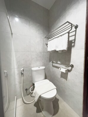 A bathroom with a toilet, a shower, and a towel rack. - RUKUN Place Bandung  (Kota Bandung)