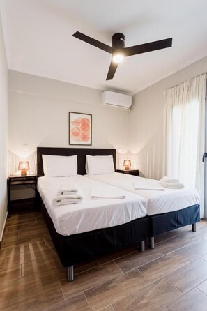 Una cama doble con cabecera negra, dos mesitas de noche con lámparas, un ventilador de techo y un cuadro enmarcado en la pared.