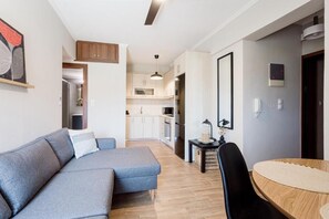 Una sala de estar moderna con un sofá seccional gris, una mesa redonda de madera y una cocina al fondo.