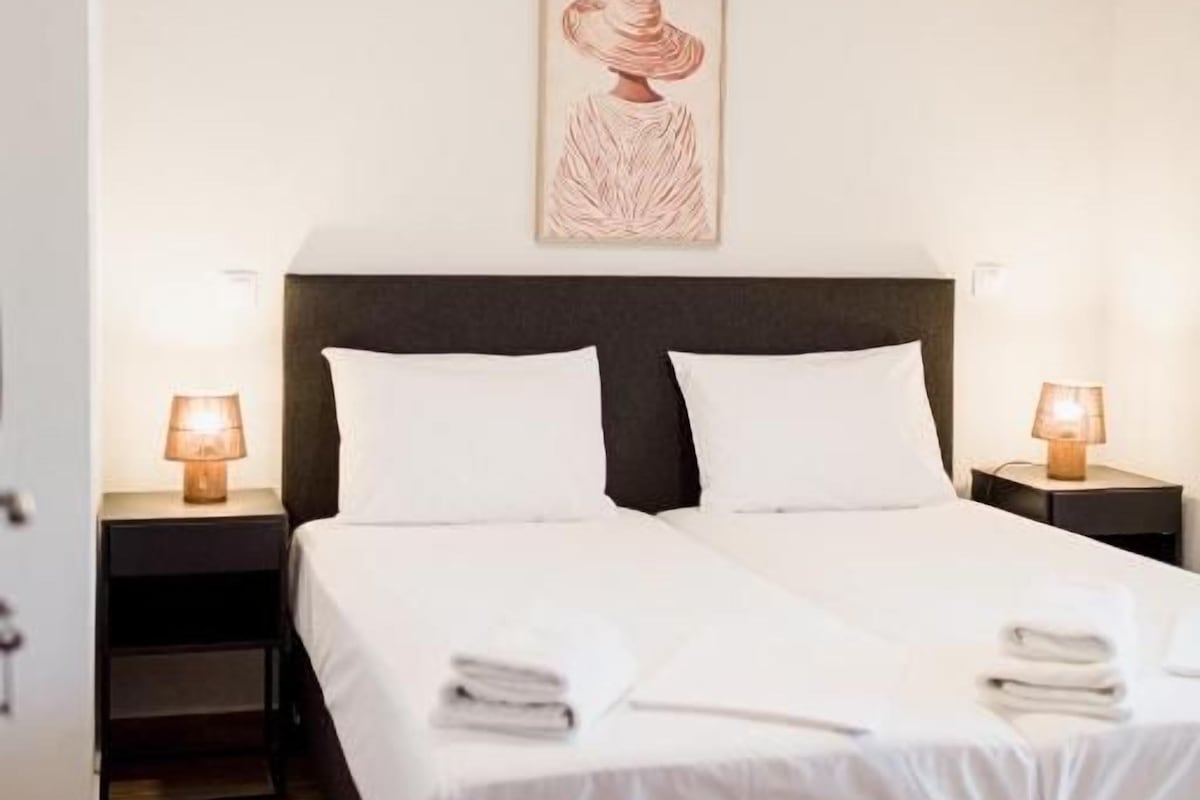 Habitación de hotel con una cama, dos mesitas de noche, un velador, un ventilador de techo y un cuadro en la pared.