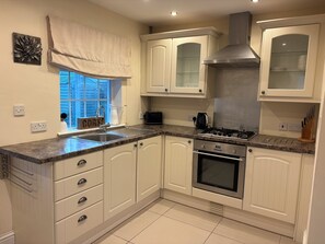 A kitchen with white cabinetry, a stainless steel range hood, a built-in oven, and a window with a view of the outside.