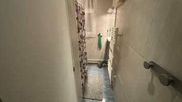 A narrow hallway with a tiled floor, a door on the right, and a window with a curtain at the end.