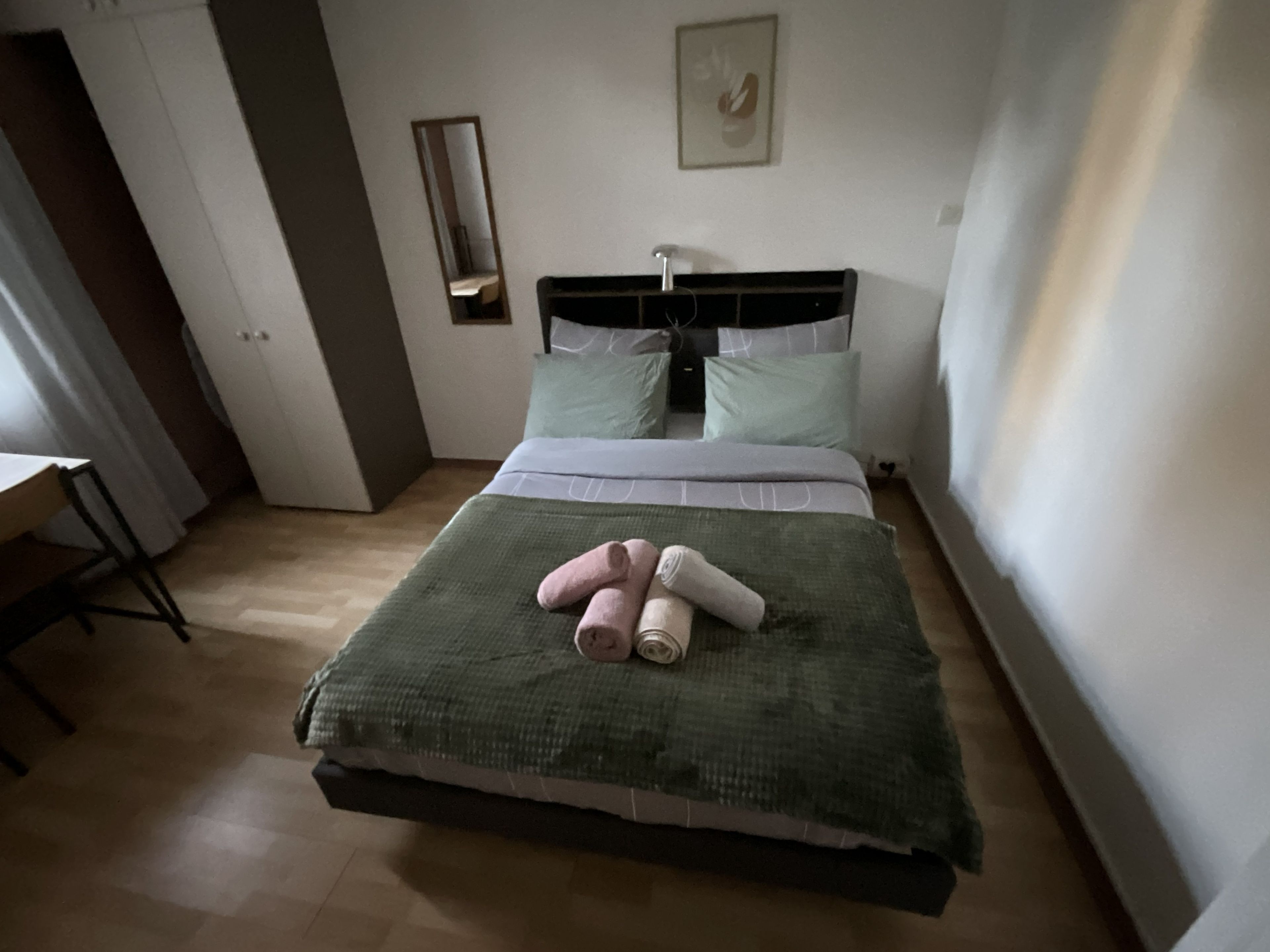 Een slaapkamer met een bed, kussens, een spiegel en een nachtkastje.