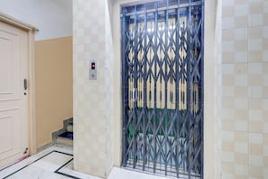 Une pièce dotée d’une porte, d’un panneau de commande d’ascenseur fixé au mur et d’une grille métallique.