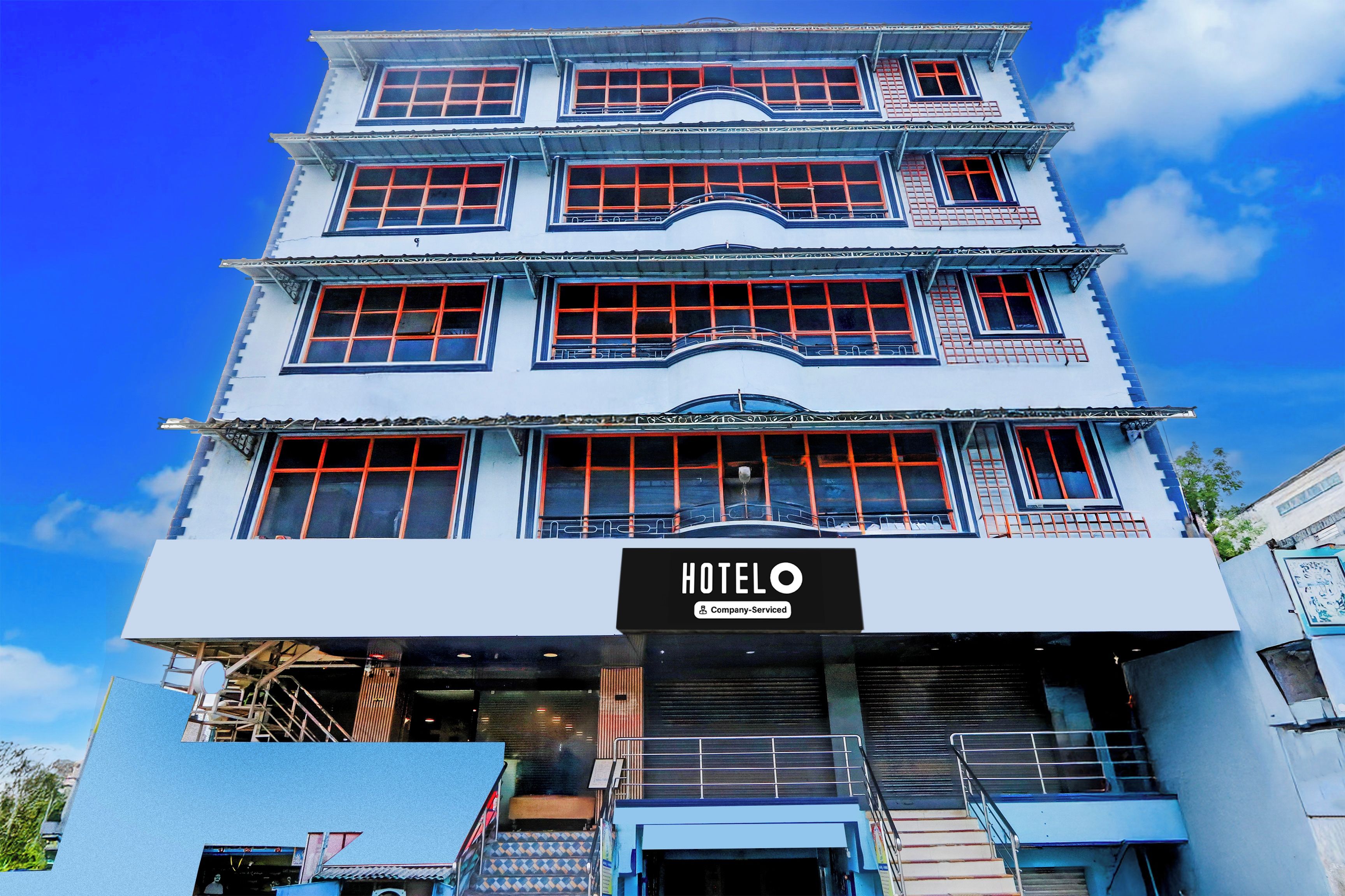 Un hotel de varios pisos con un llamativo letrero 'HOTELO', amplias ventanas y una escalera que lleva a la entrada.