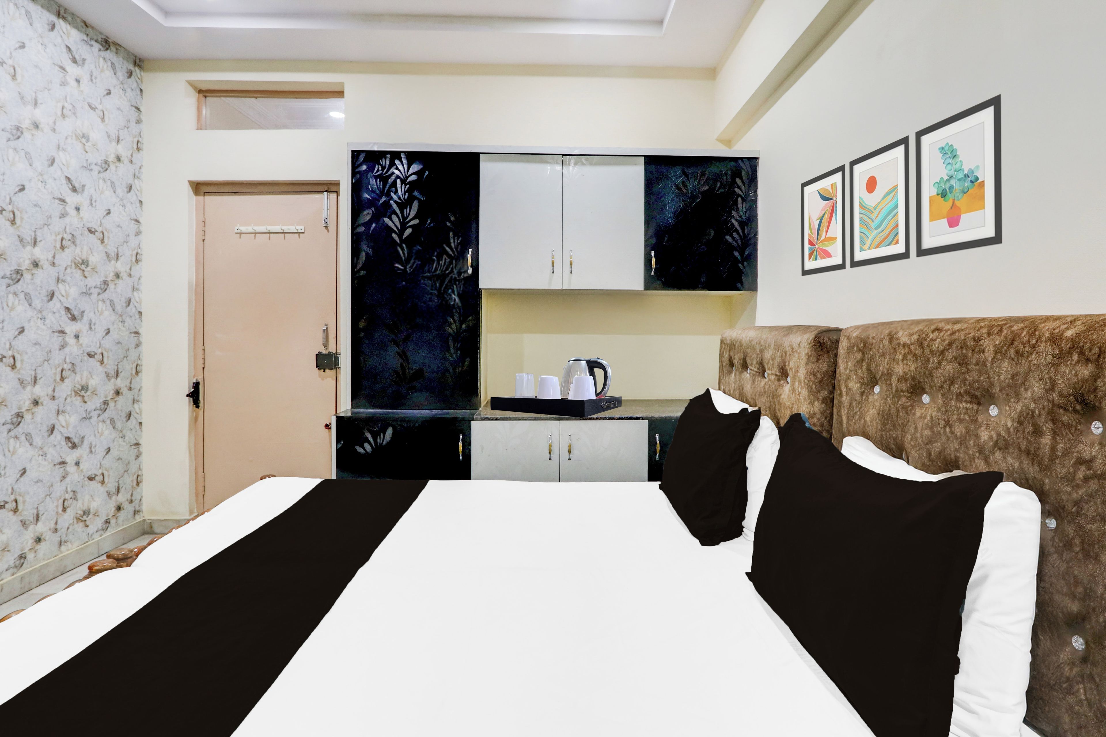 Una habitación de hotel con una cama grande, una kitchenette, una puerta y una pared decorada con cuadros.
