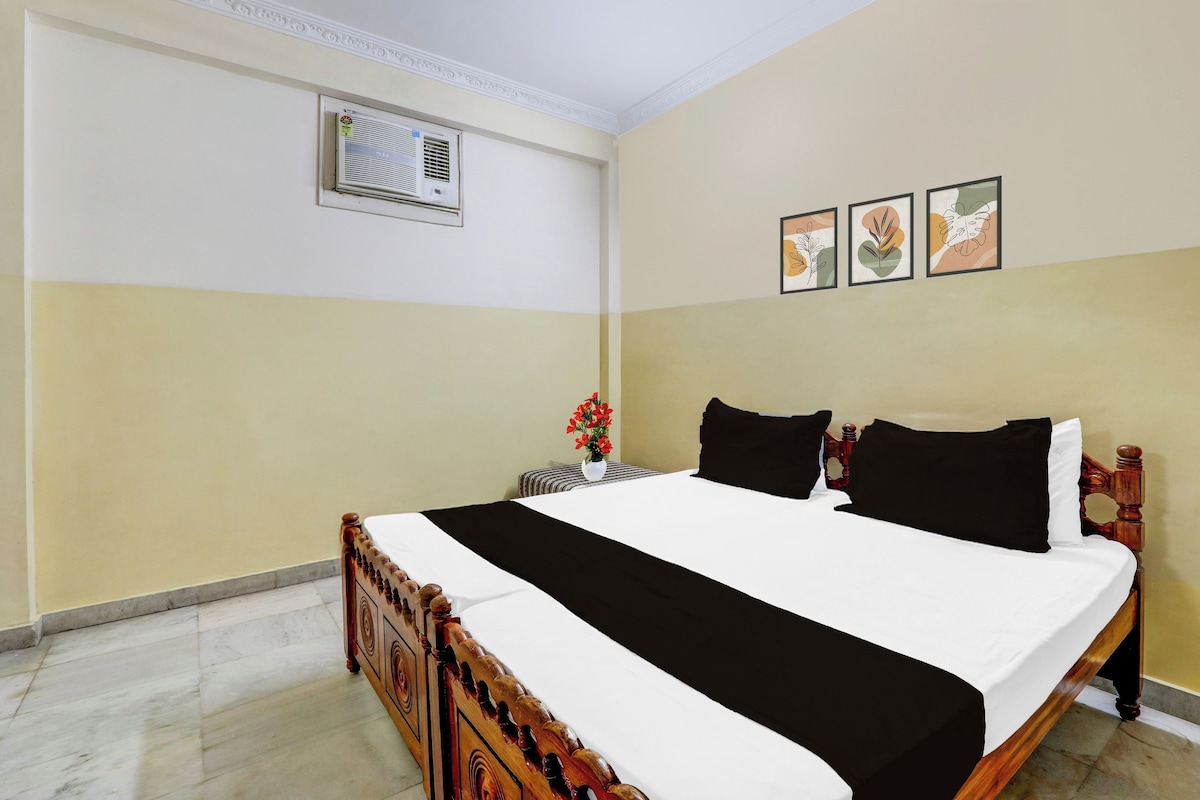 Une chambre d’hôtel comprenant un lit, une table de chevet, un climatiseur fixé au mur et trois tableaux encadrés.