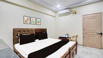 A neatly made bed with a headboard, a bedside table with a kettle and cups, and a door to the right.