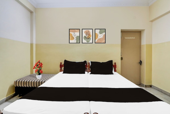 Une chambre d’hôtel avec un grand lit, une table de chevet ornée d’un vase de fleurs et trois tableaux encadrés accrochés au mur.