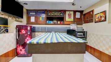A room with a bed, a refrigerator, a television, and a wall-mounted shelf with various items.