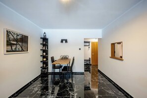 Ein Essbereich mit Tisch und Stühlen, einem schwarzen Marmorboden, einem an der Wand befestigten Regal mit Dekoration und einem Gemälde.