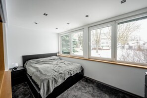 Ein Schlafzimmer mit Bett, Nachttisch und einem Fenster mit Blick auf eine verschneite Landschaft.