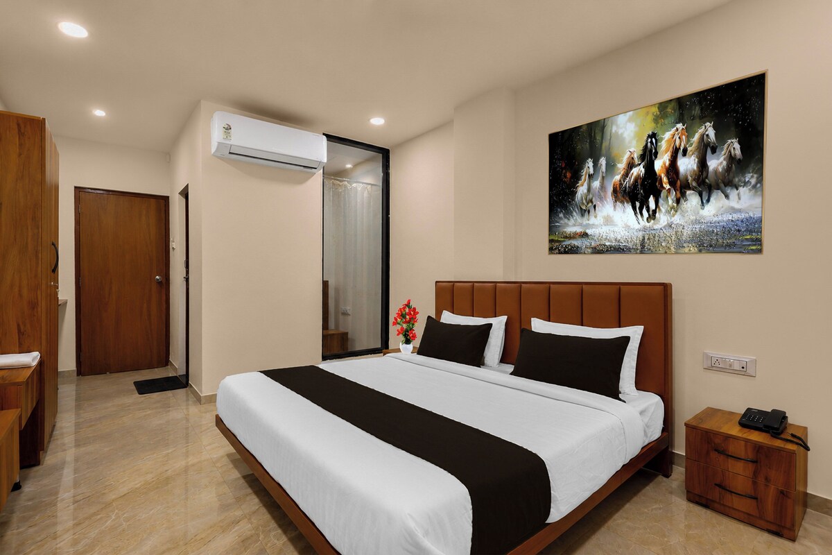 Una habitación de hotel con una cama grande, un cuadro de caballos, un equipo de aire acondicionado y una mesita de noche de madera.