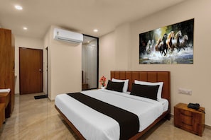 Una habitación de hotel con una cama grande, un cuadro de caballos, un equipo de aire acondicionado y una mesita de noche de madera.