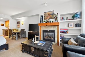 A modern living room with a fireplace, a television, a bookshelf, and a dining area. - Steps To Winter Park Gondola • Shared Hot Tub + Pool | Little Moose (Winter Park)