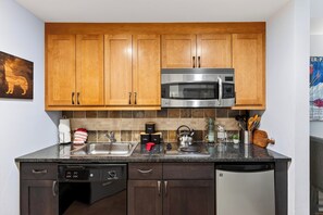A compact kitchen with wooden cabinets, a stainless steel microwave, a coffee maker, and a kettle. - Steps To Winter Park Gondola • Shared Hot Tub + Pool | Little Moose (Winter Park)