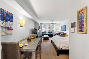 A hotel room with a bed, a desk with a chair, a TV, a ceiling fan, and a poster on the wall. - Steps To Winter Park Gondola • Shared Hot Tub + Pool | Little Moose (Winter Park)