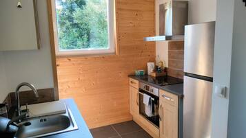 Eine kleine Küche mit Fenster, Holzwänden, einem Edelstahlkühlschrank und einer Spüle.